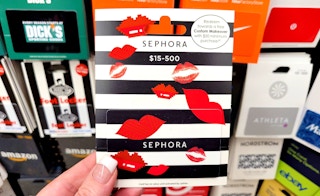A person's hand holding a Sephora gift card in front of a display of gift cards.