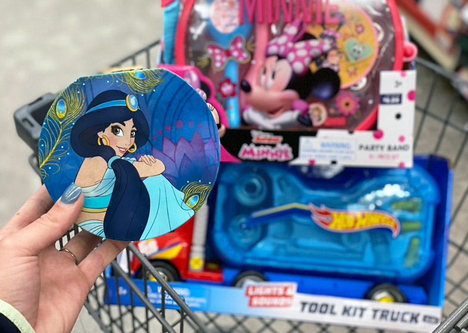 A person's hand holding a Disney toy in front of more toys sitting in a Walgreens shopping cart.