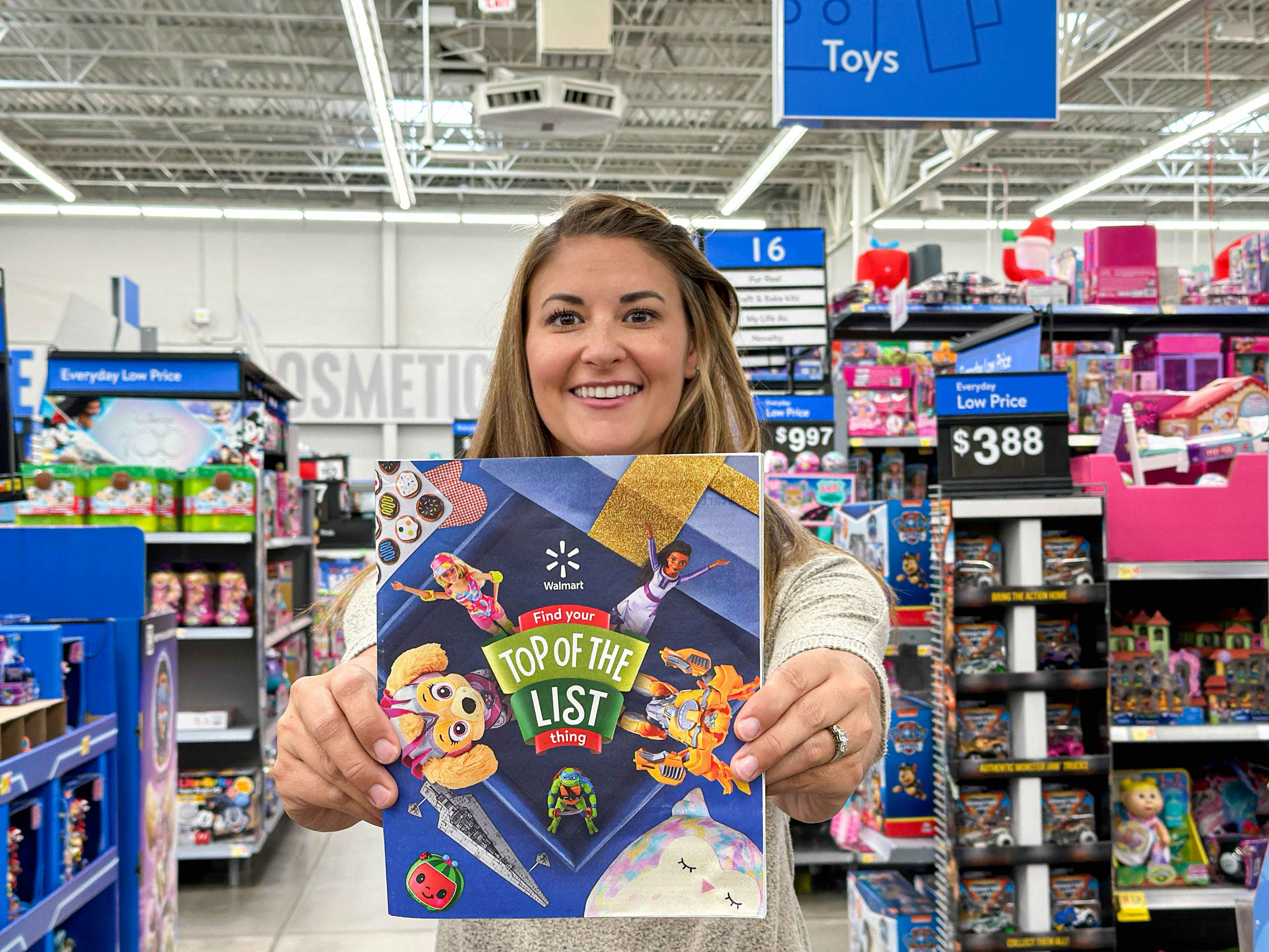 a woman standing in Walmart and smiling while holding up the 2023 toy catalog