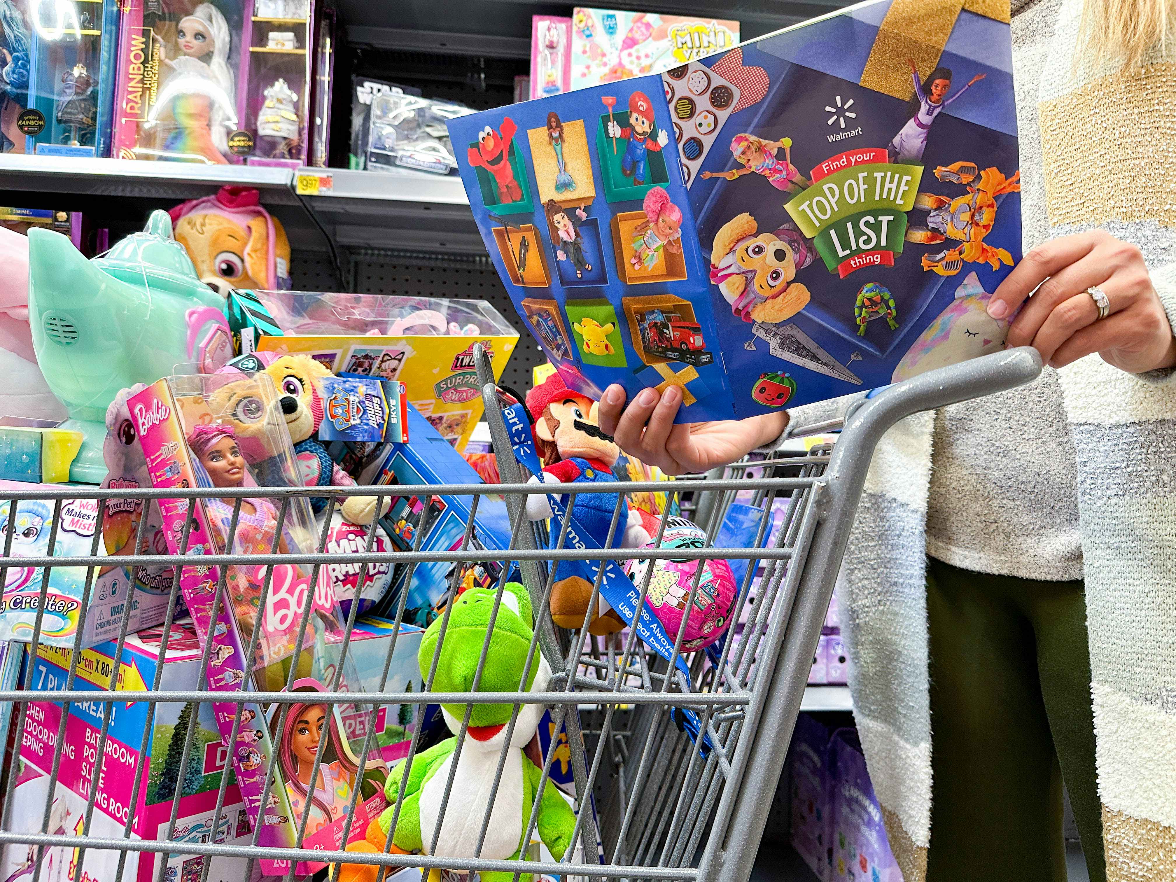 a person looking at the walmart toy catalog in store with a full cart of toys 