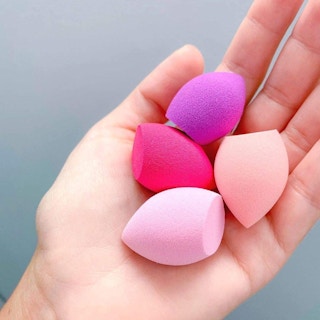 A hand holding four Real Techniques beauty sponges.