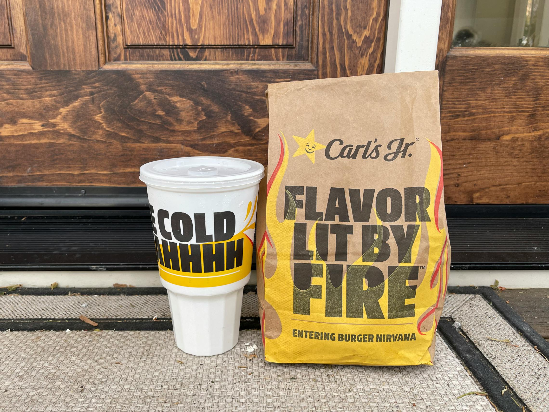 Carl's Jr take out bag and drink sitting on a front porch.