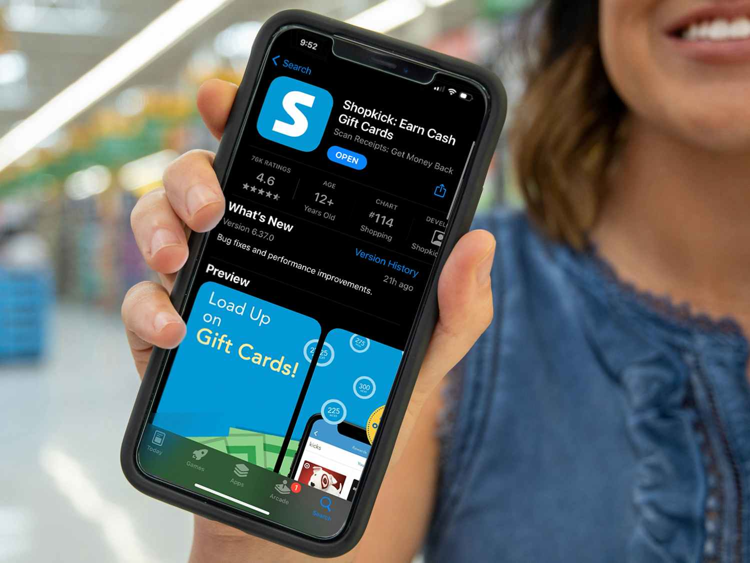 A person holding their phone up in a store, showing the app store download screen for Shopkick