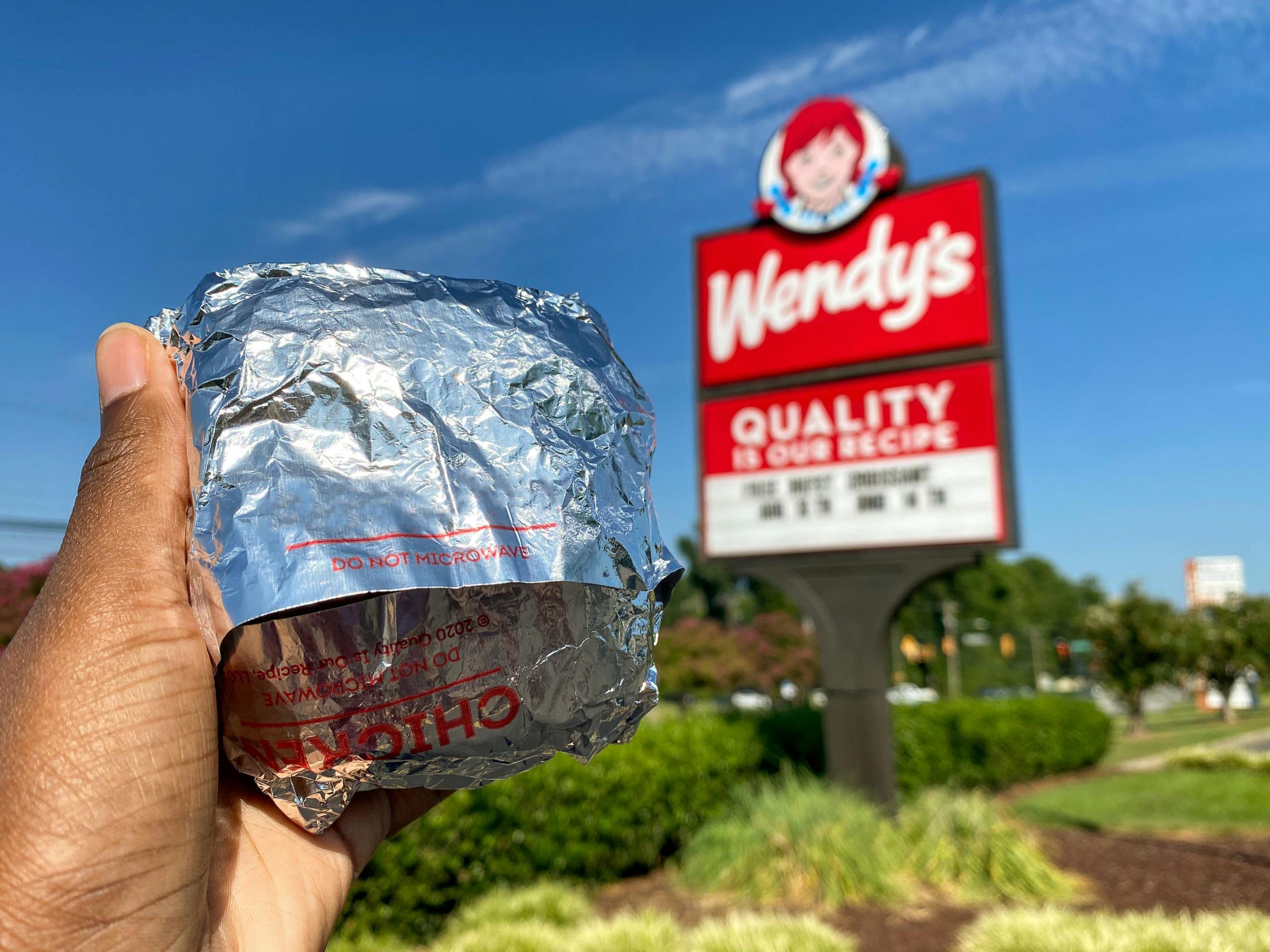 A person holding up a Wendy's breakfast sandwich in front of a Wendy's sign