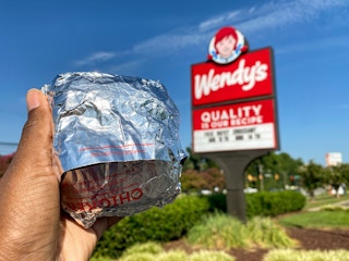 A person holding up a Wendy's breakfast sandwich in front of a Wendy's sign