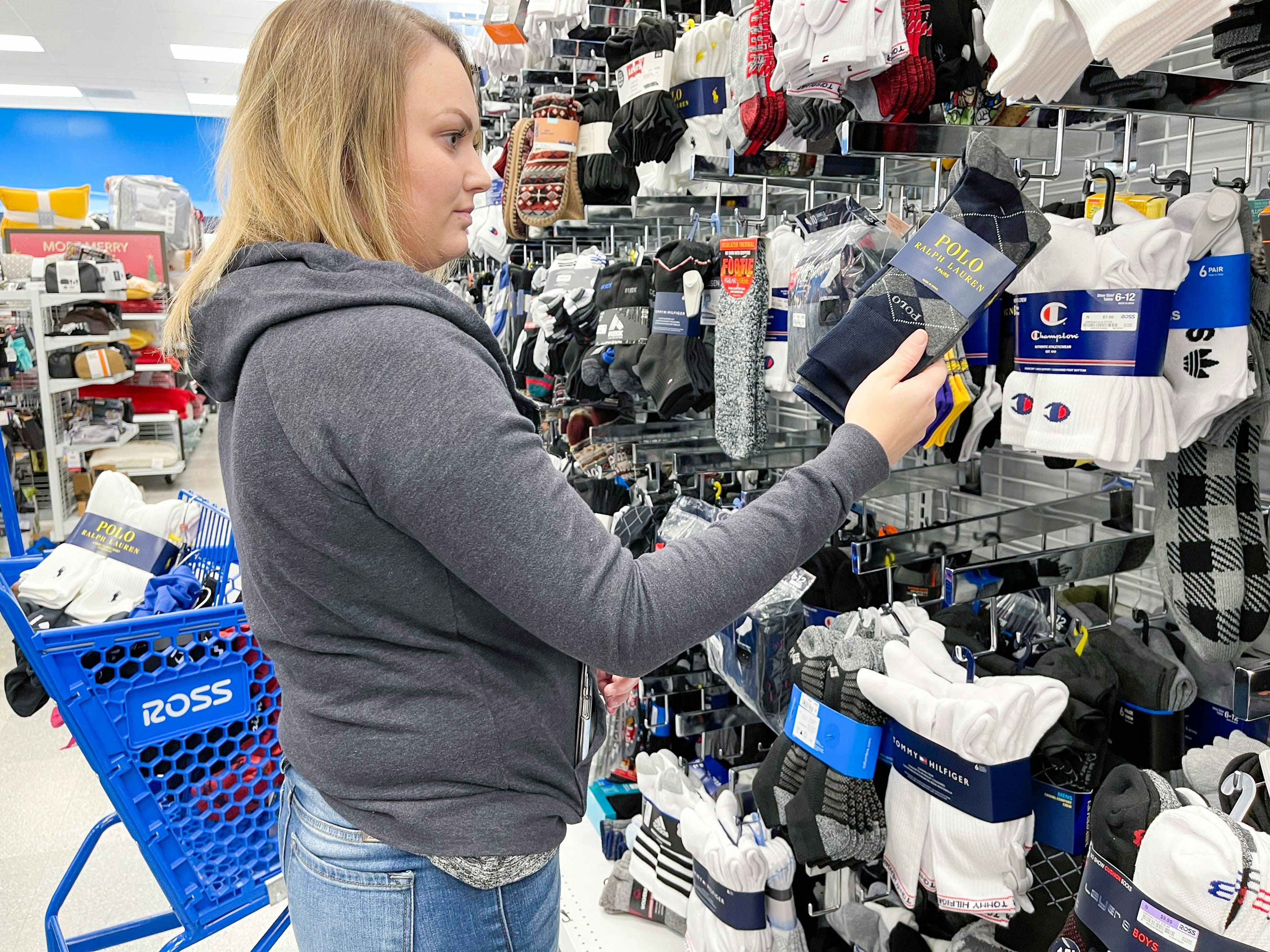 A woman looking at socks with a Ross shopping cart beside her.