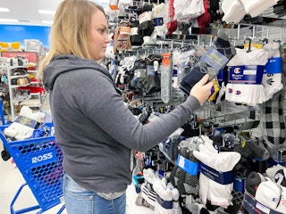 A woman looking at socks with a Ross shopping cart beside her.