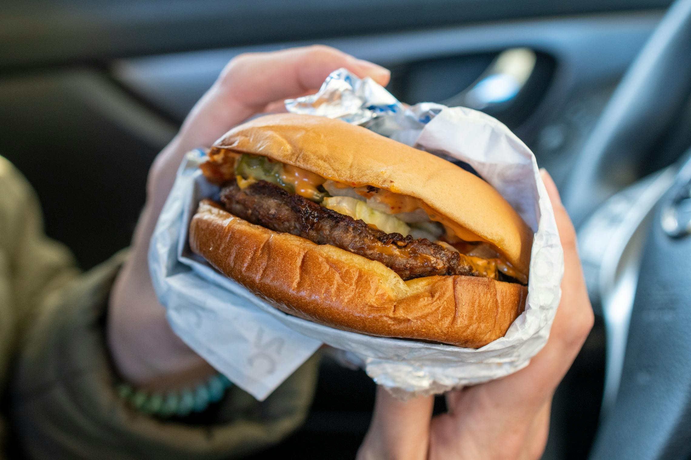 A close up of a sonic cheeseburger held in a car