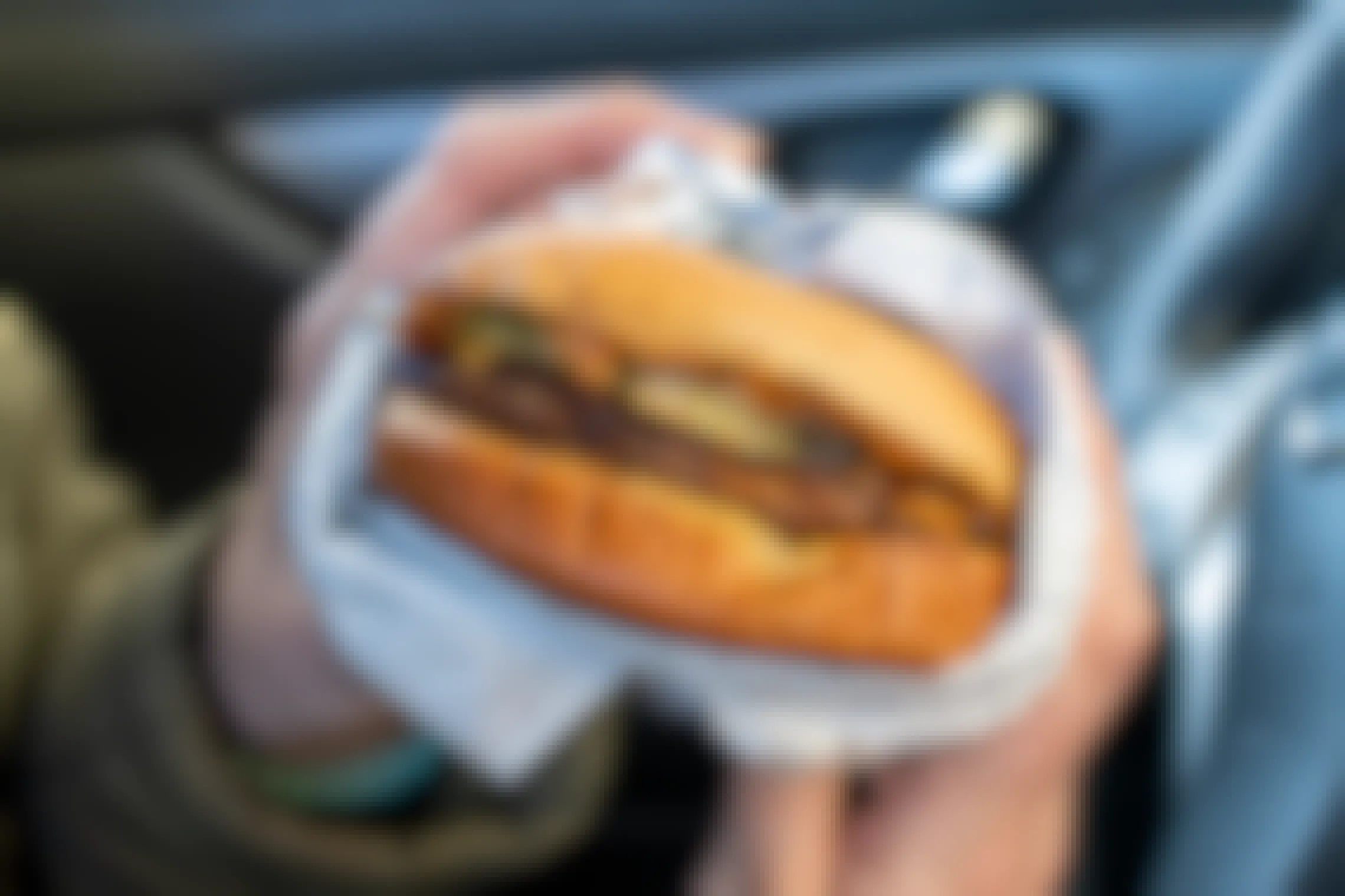 A close-up of a Sonic cheeseburger being held by someone sitting in a car.