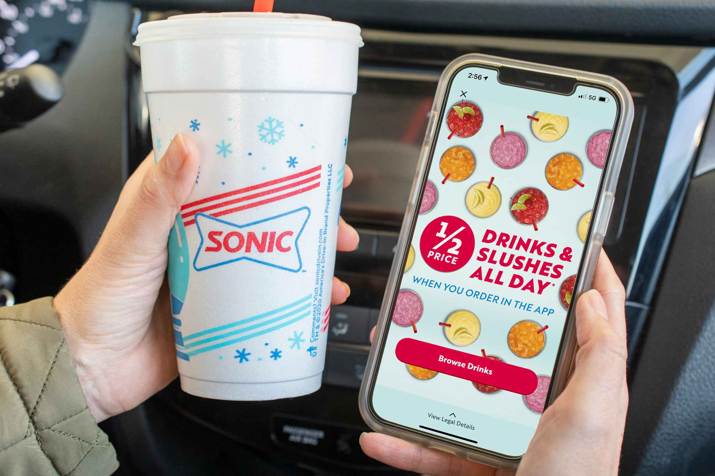A person sitting in their car, holding a Sonic drink cup next to their cell phone, displaying an advertisement for Sonic that reads, "1/2 price drinks & slushes all day when you order in the app