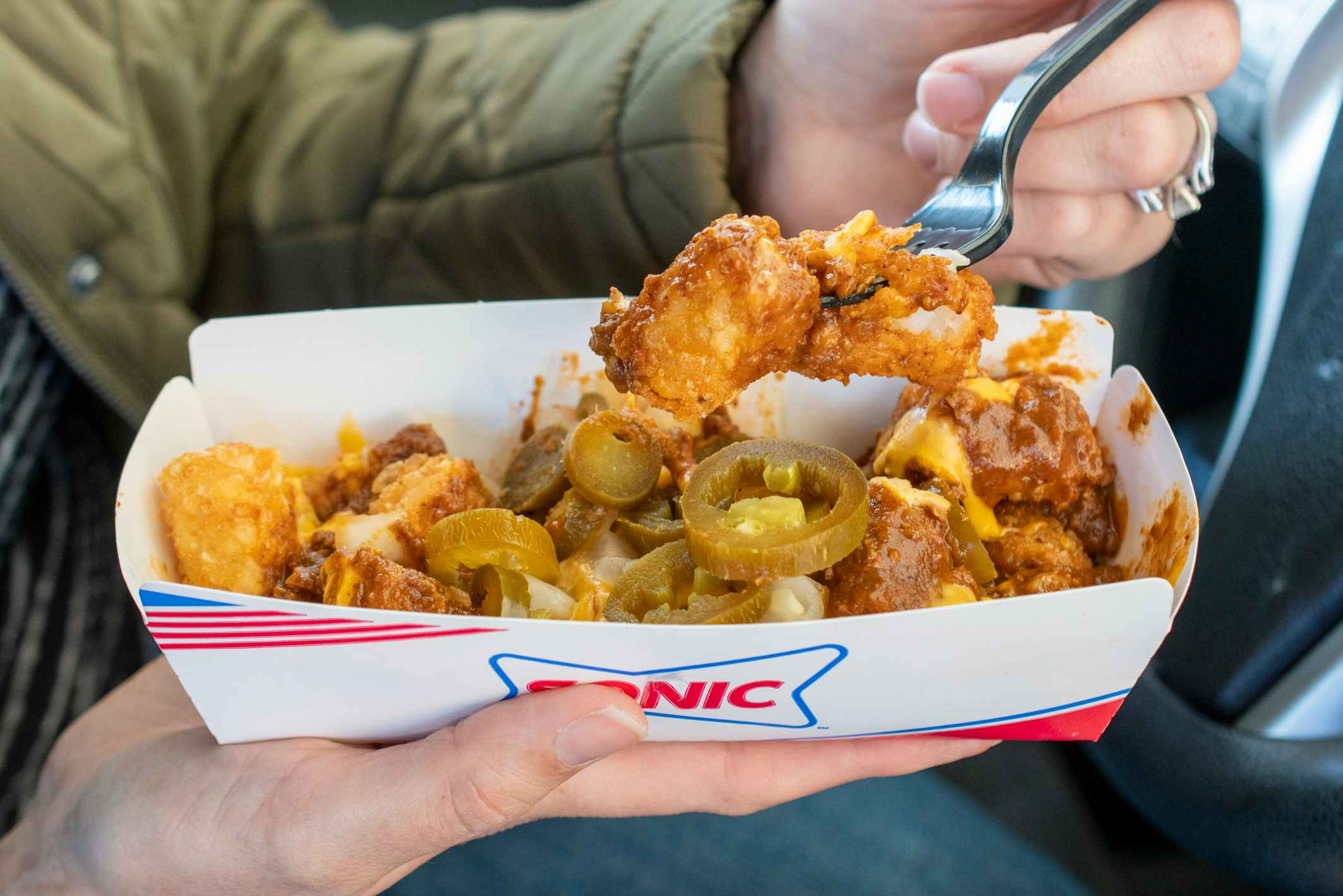 A person scooping a bite full of Sonic loaded tots from a cardboard fast food dish.