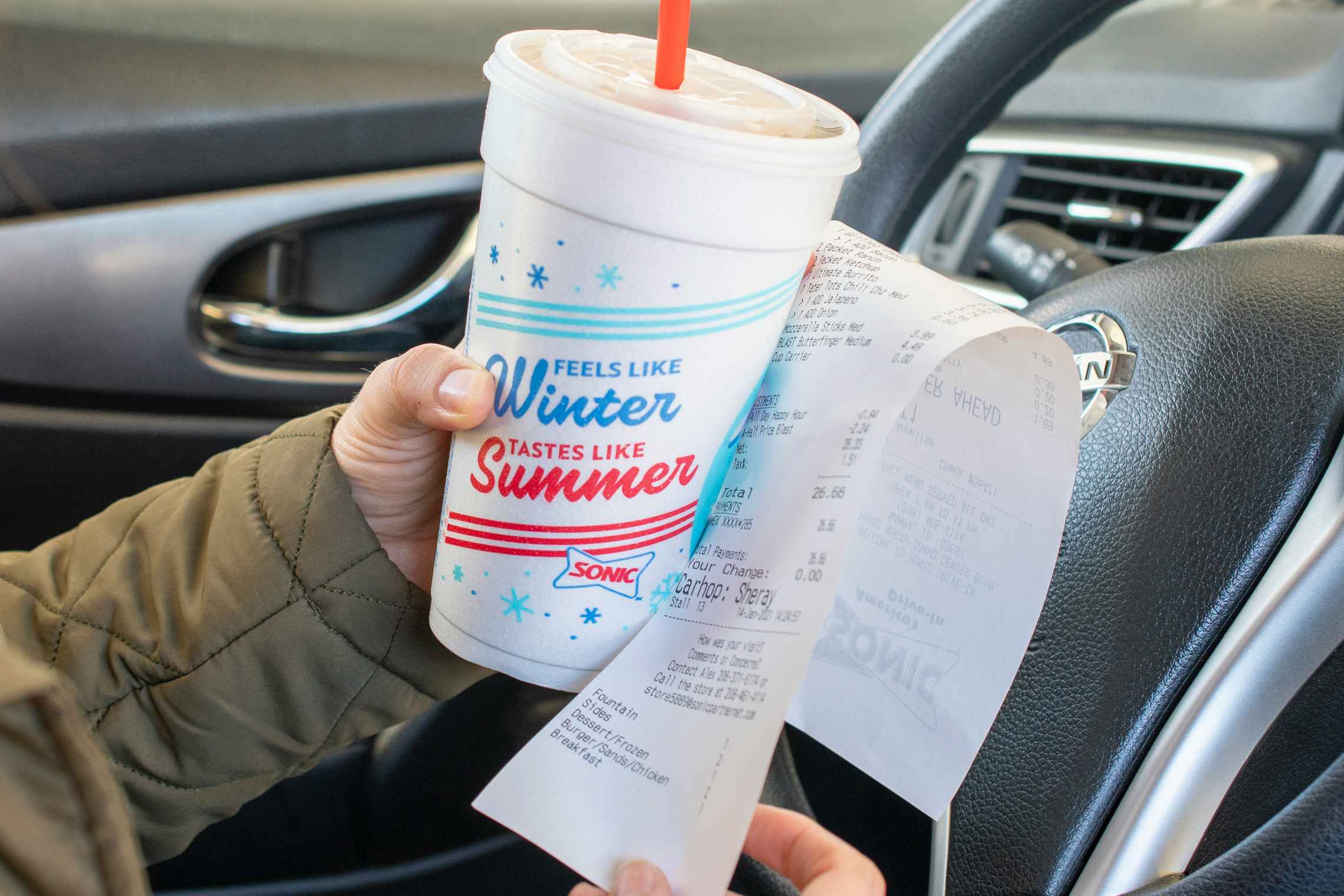 A person holding a Sonic receipt next to a Sonic beverage while sitting in a car.