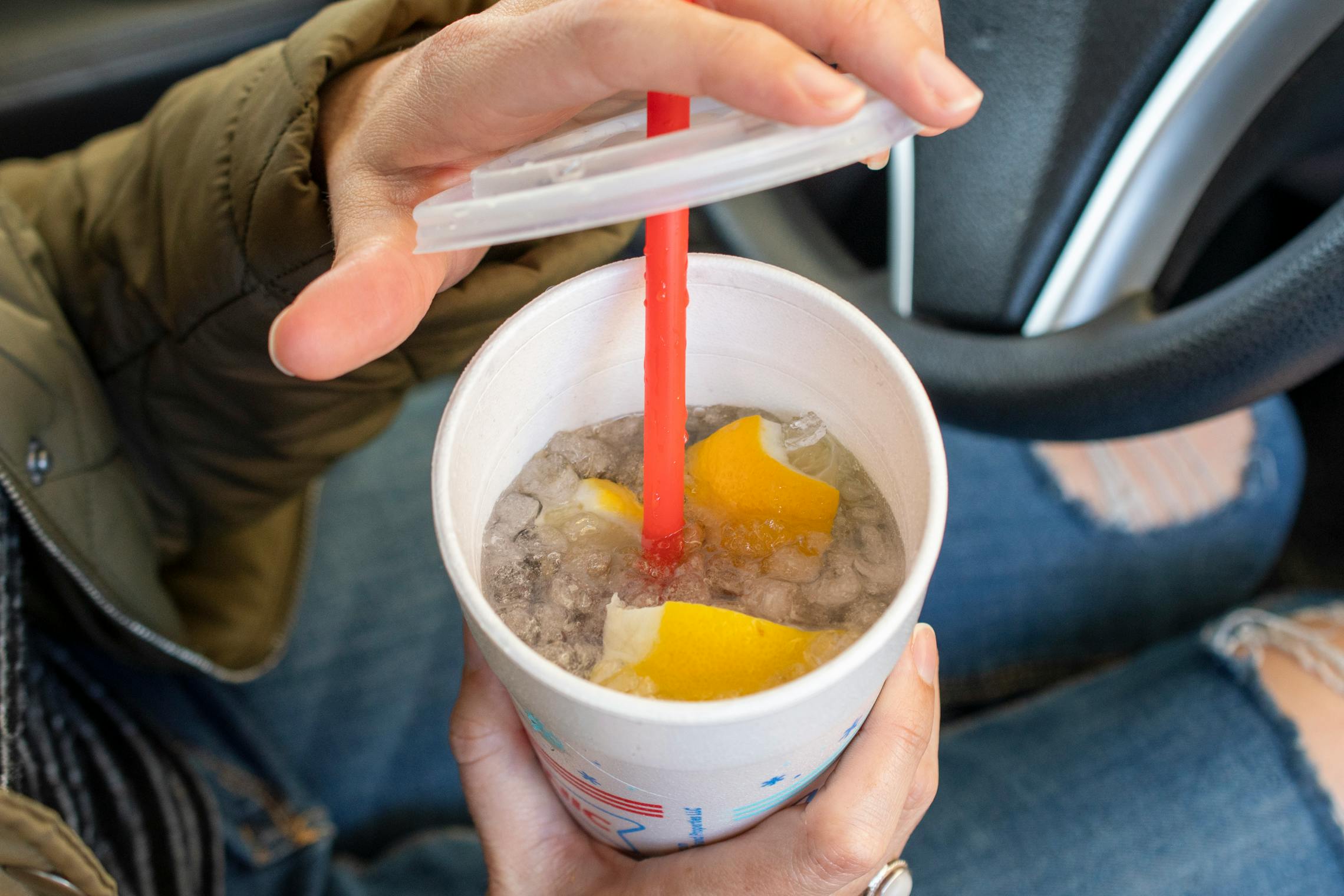 A person taking the lid off of a Sonic drink cup, showing the inside with ice, lemon, and their purple drink.