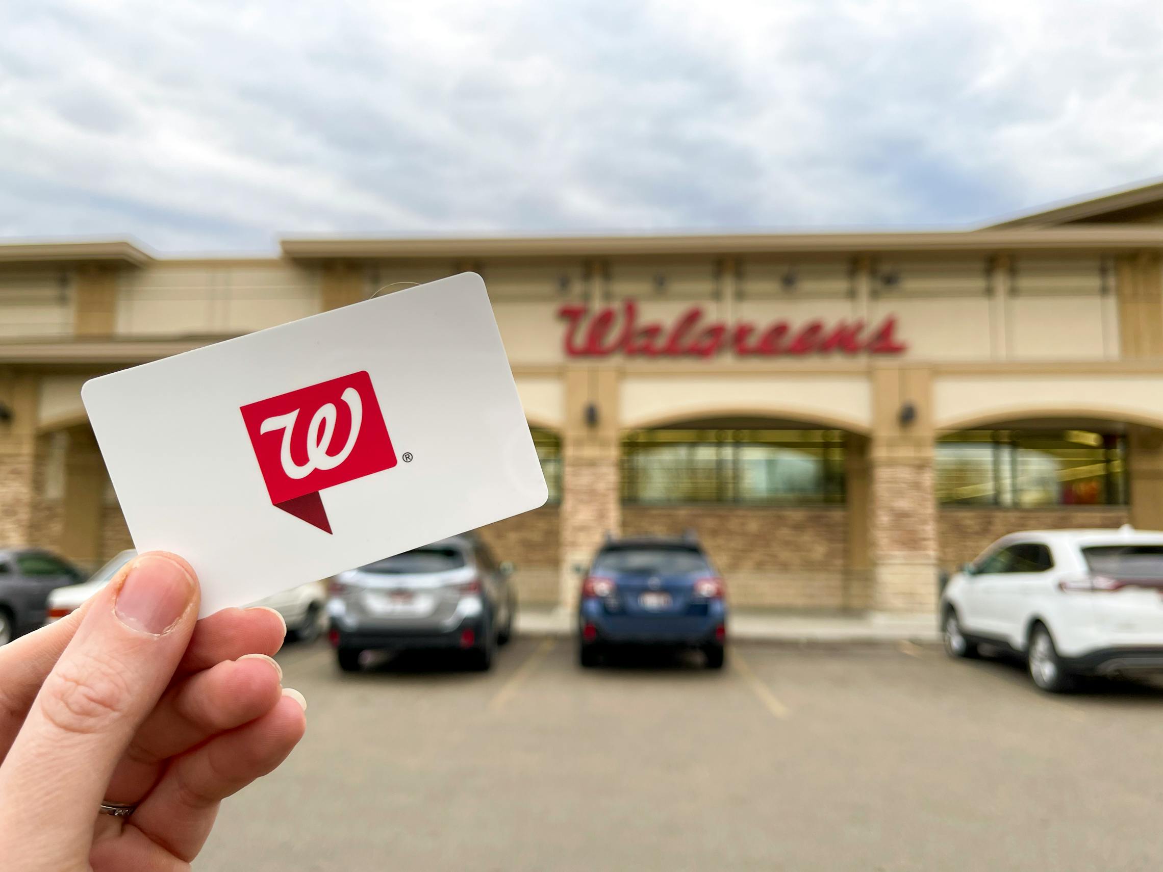 A person holding a Walgreens gift card in front of Walgreens.