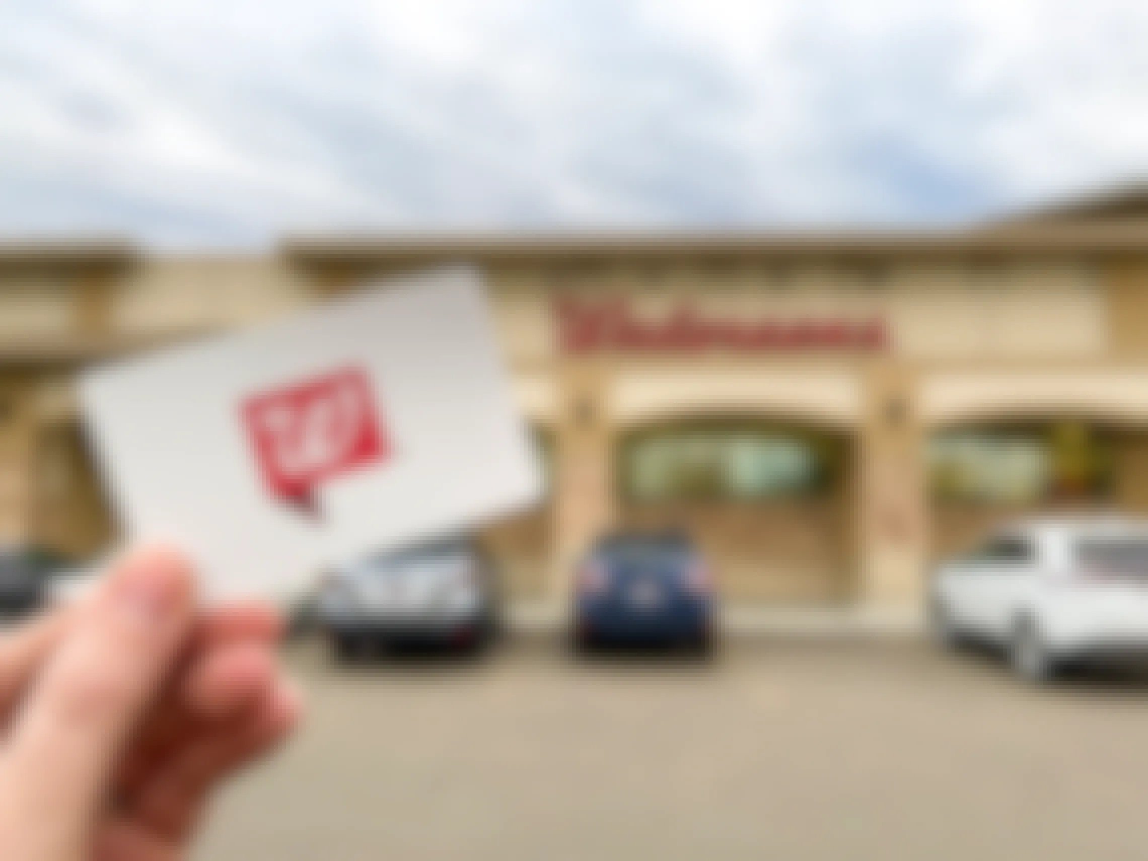 A person holding a Walgreens gift card in front of Walgreens.