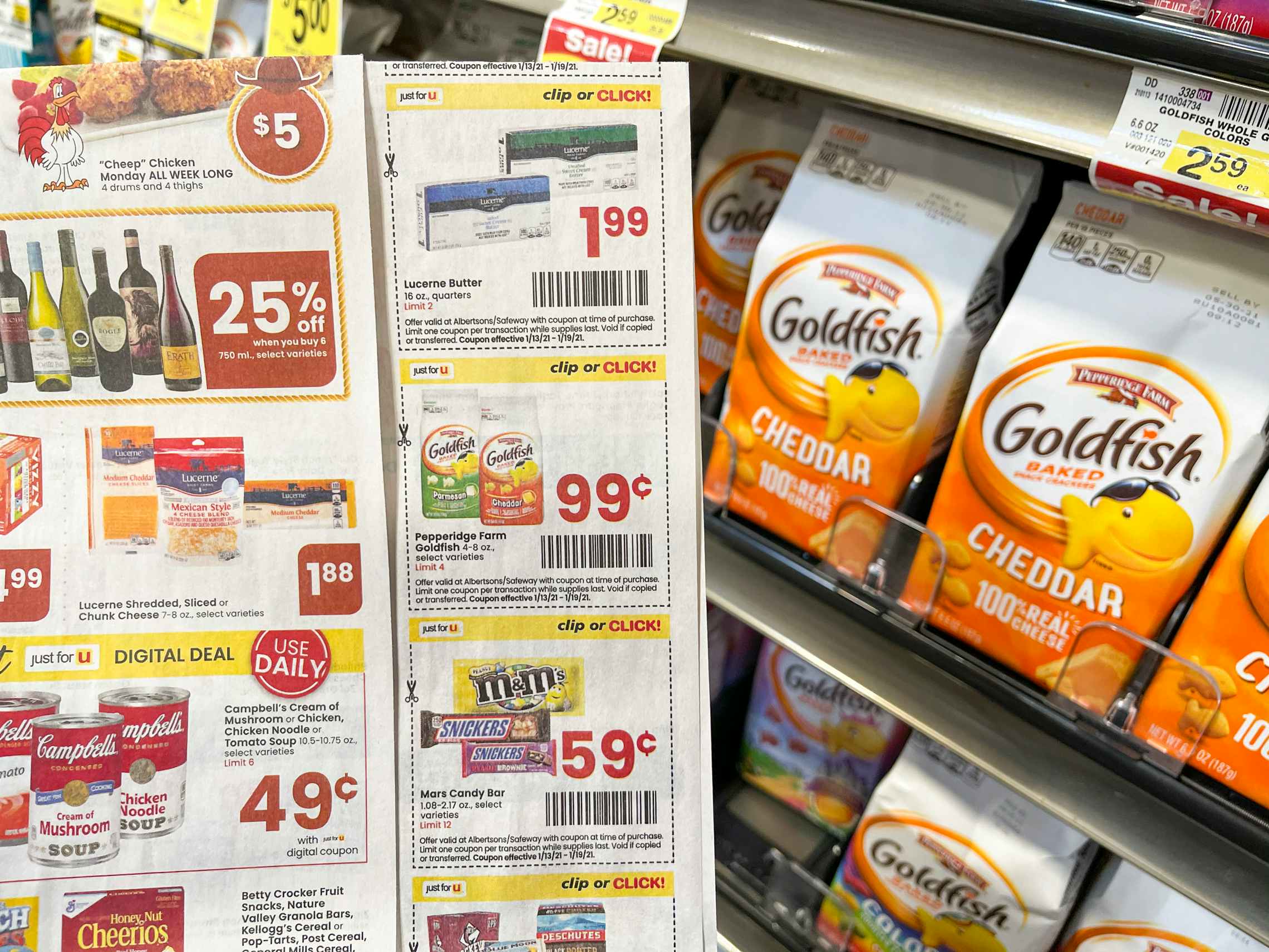 A page of coupons being held up next to a shelf with bags of Goldfish crackers.