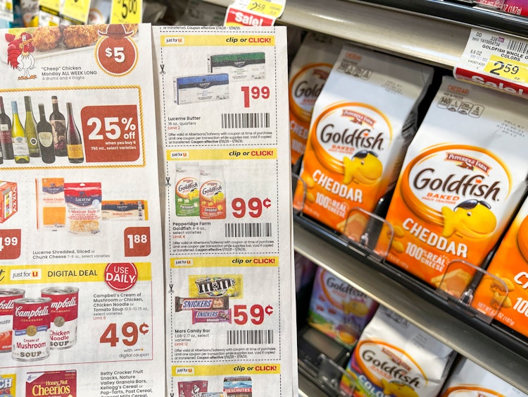 A page of coupons being held up next to a shelf with bags of Goldfish crackers.