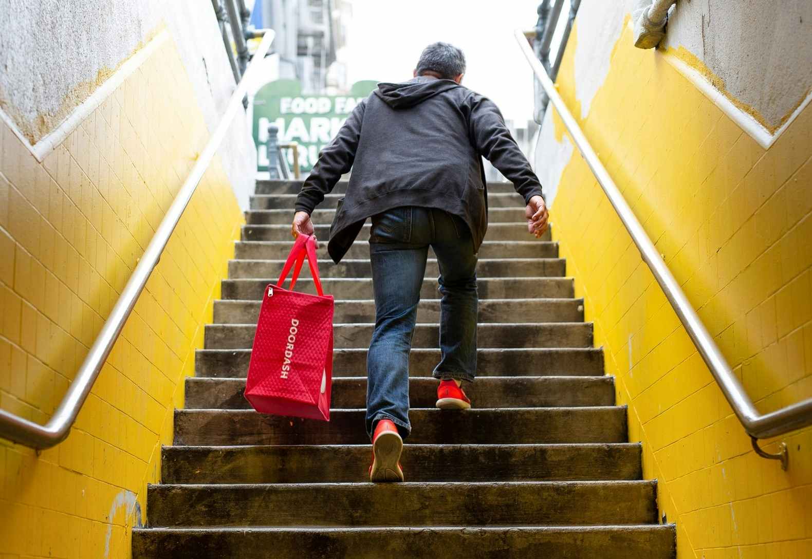 A man walking up some stairs carrying a DoorDash bag.