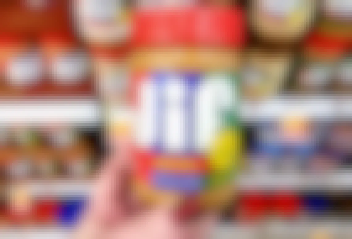 A person holding a ja of Jif peanut butter in fornt of a store shelf with other jars of Jif peanut butter.