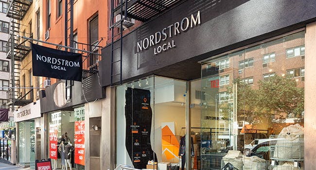 A Nordstrom Local storefront with a hanging sign on a street of stores.