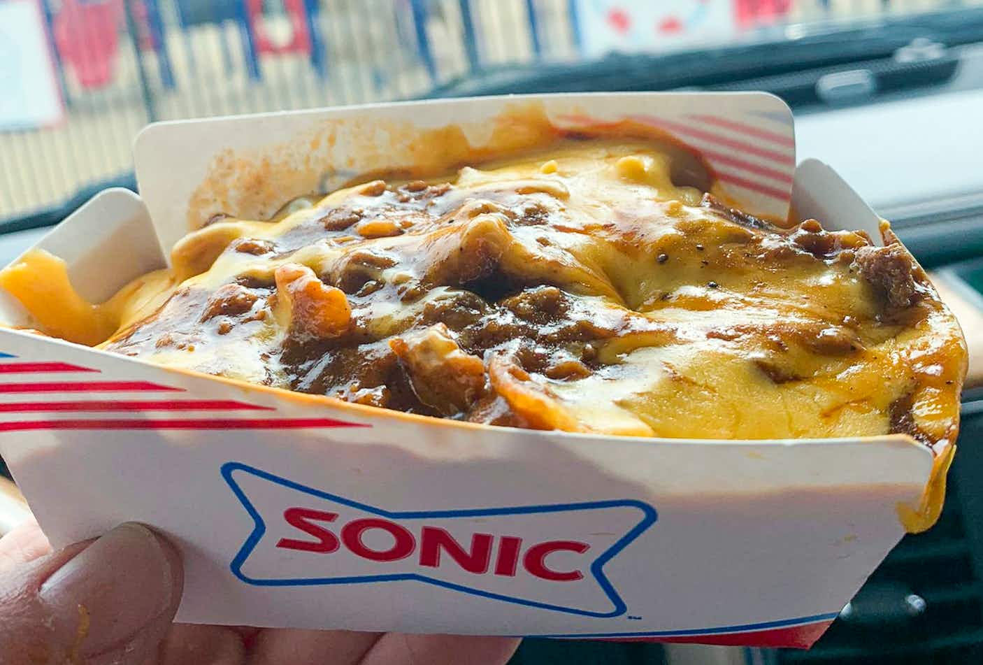 A person's hand holding up a container of a Sonic Drive-in secret menu item: Frito Chili Pie.