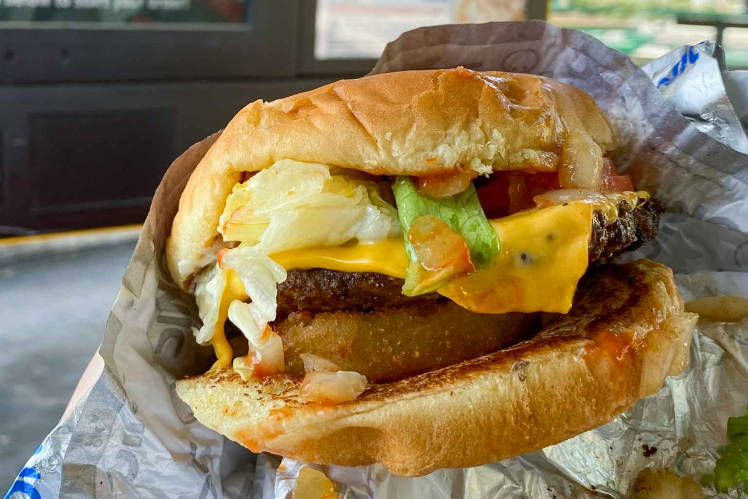 A close-up of a Sonic cheeseburger with onion rings added to it.