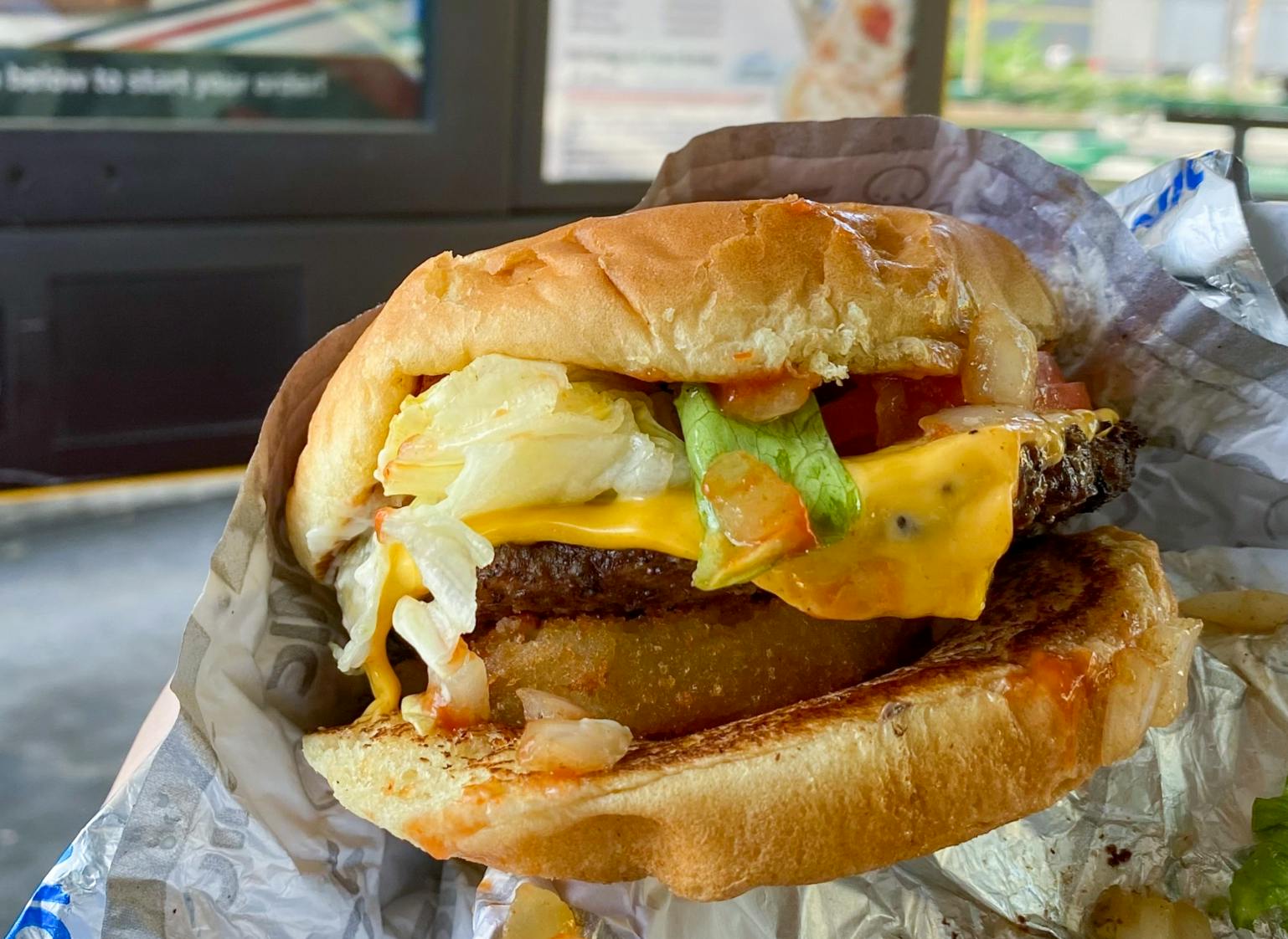 A close-up of a Sonic cheeseburger with onion rings added to it.
