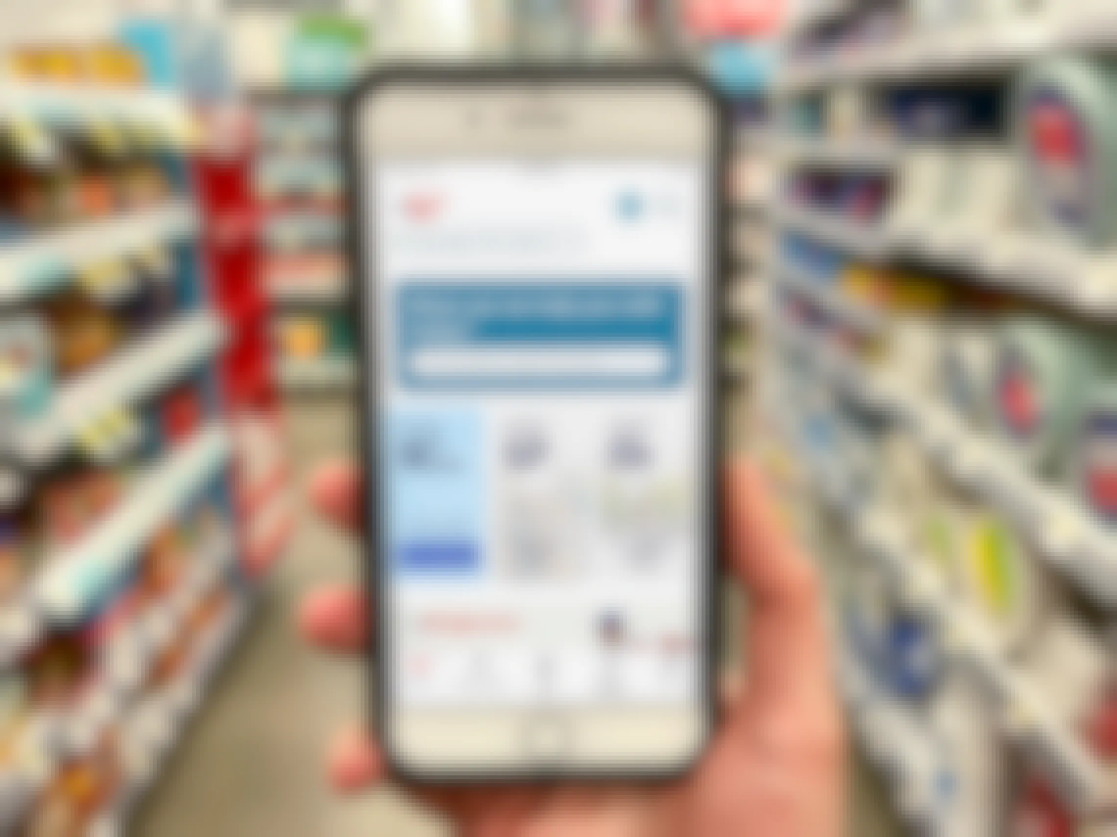 A person holding up a cell phone displaying the Walgreens app in one the drug stores' aisles