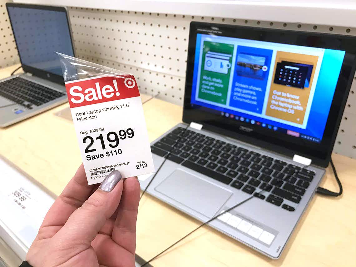 A person's hand holding up a sale tag for an Acer Laptop Chromebook in front of the display Chromebooks at Target.