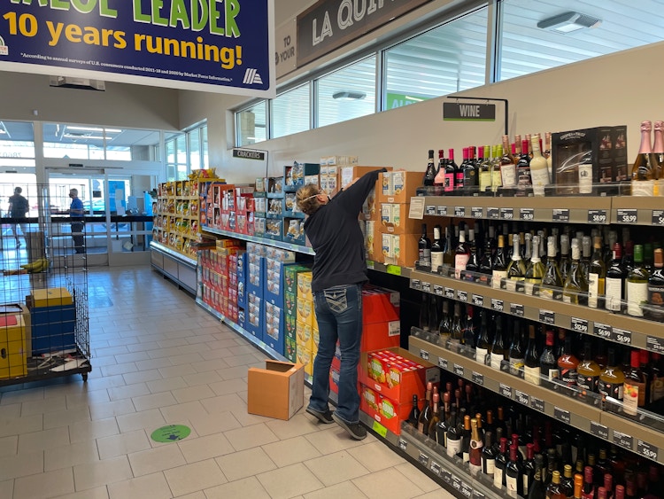 a person stocking an aldi shelf with wine 