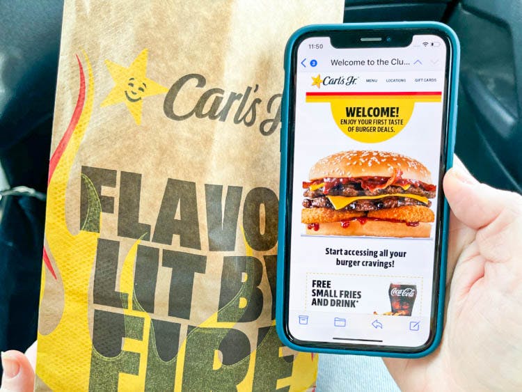 a hand holding a cell phone with carls jr app and a bag of fast food