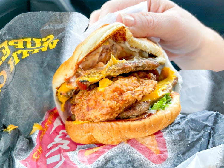 a hand opening a burger with a chicken peice on top