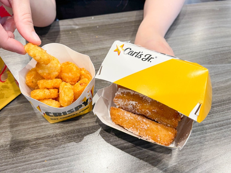 a woman grabbing a hashbrown round next to a carls jr breakfast