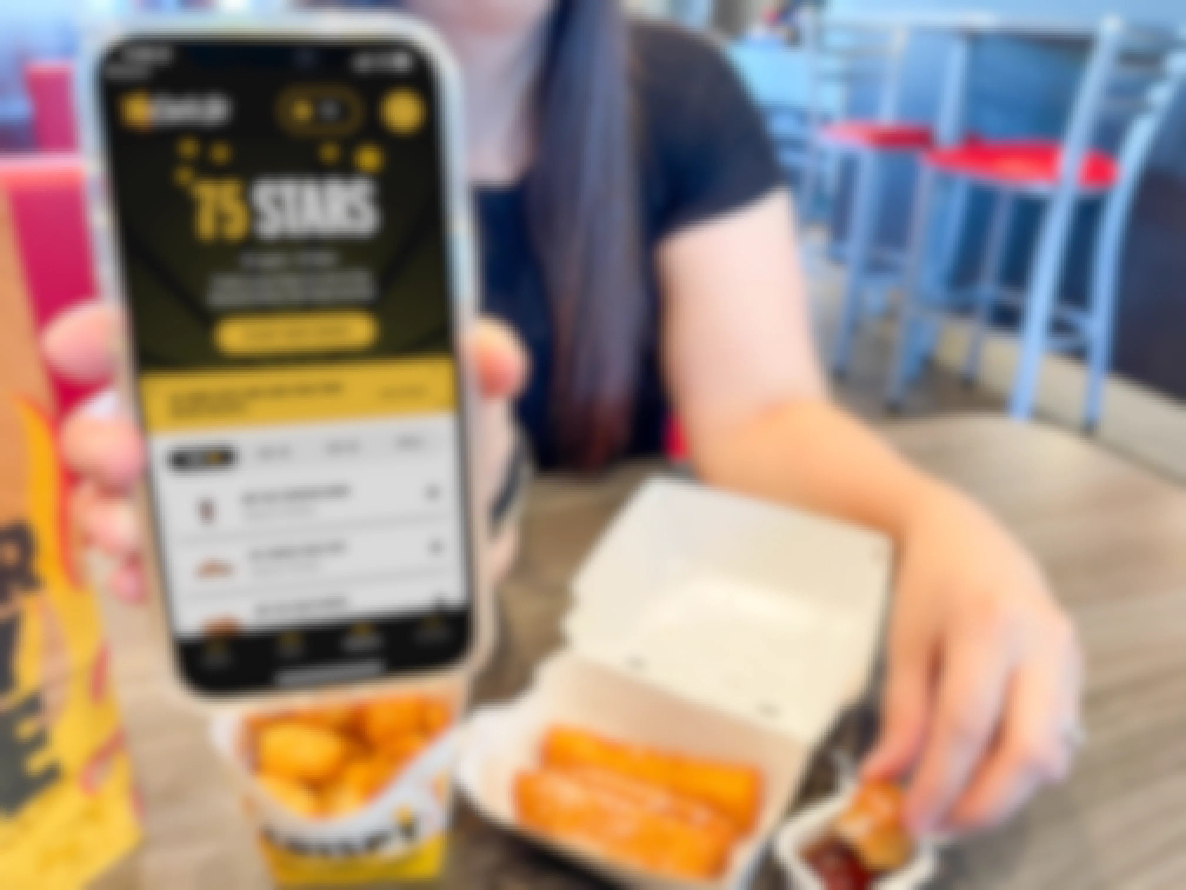 a woman grabbing a french toast sticks next to a carls jr breakfast holding a cellphone with the carls jr app