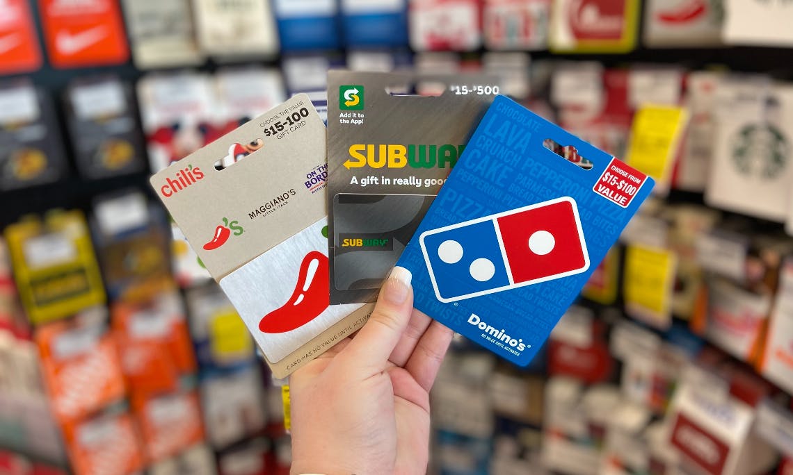 woman in CVS holding up three gift cards for Chili's, Subway, and Dominos