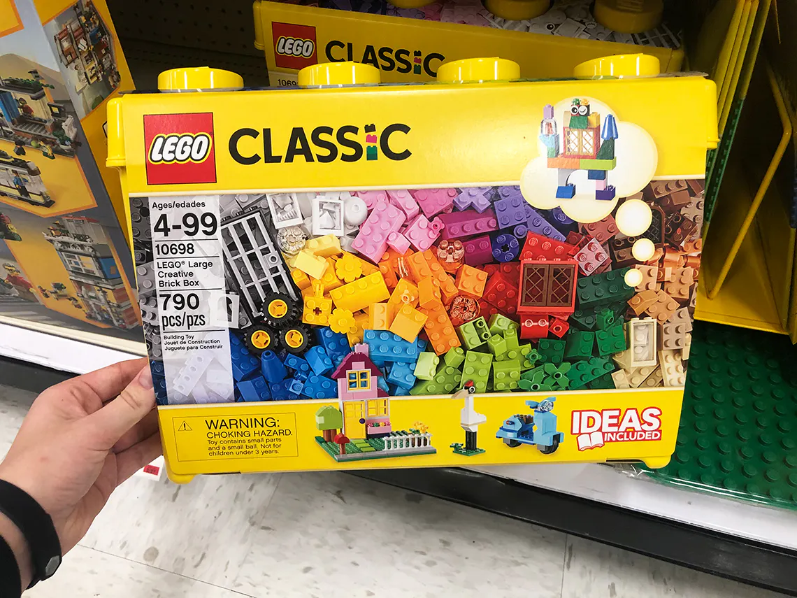 A person's hand taking a Classic LEGO box set from a shelf.