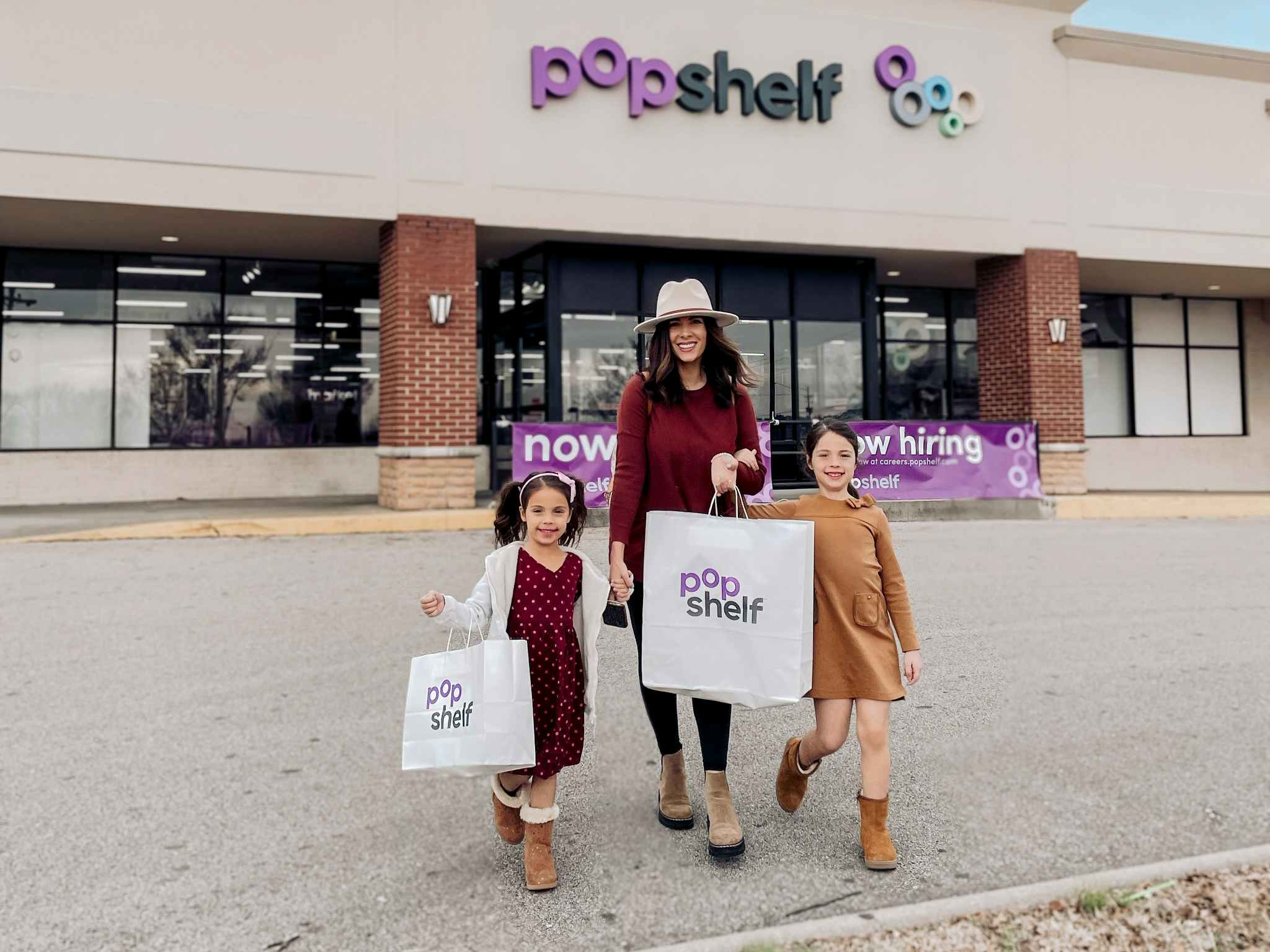 A woman with two children holding Popshelf store shopping bags, standing in front of a Popshelf store.
