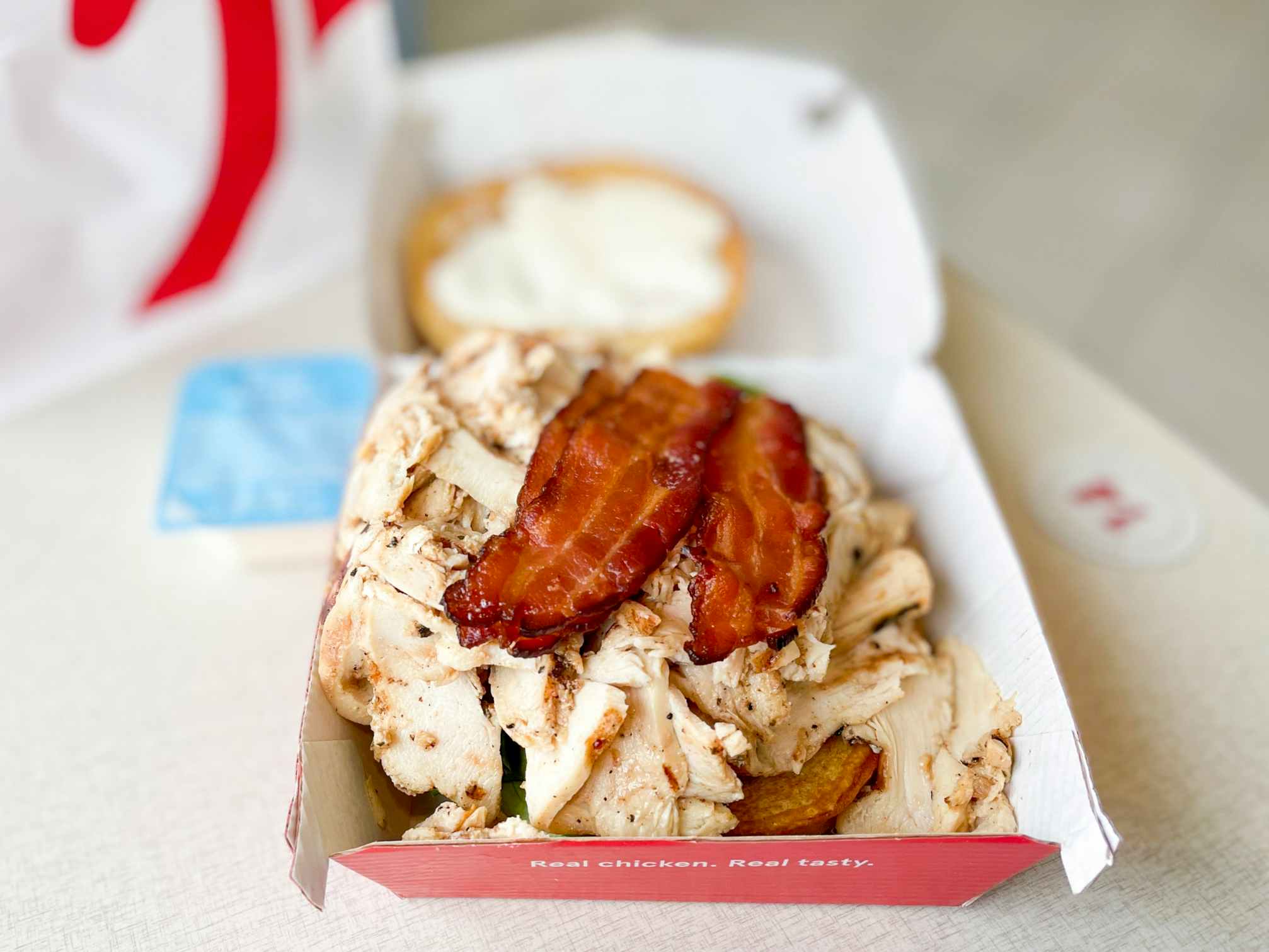 A chicken and bacon sandwich in cardboard takeout food box from chick-fil-a