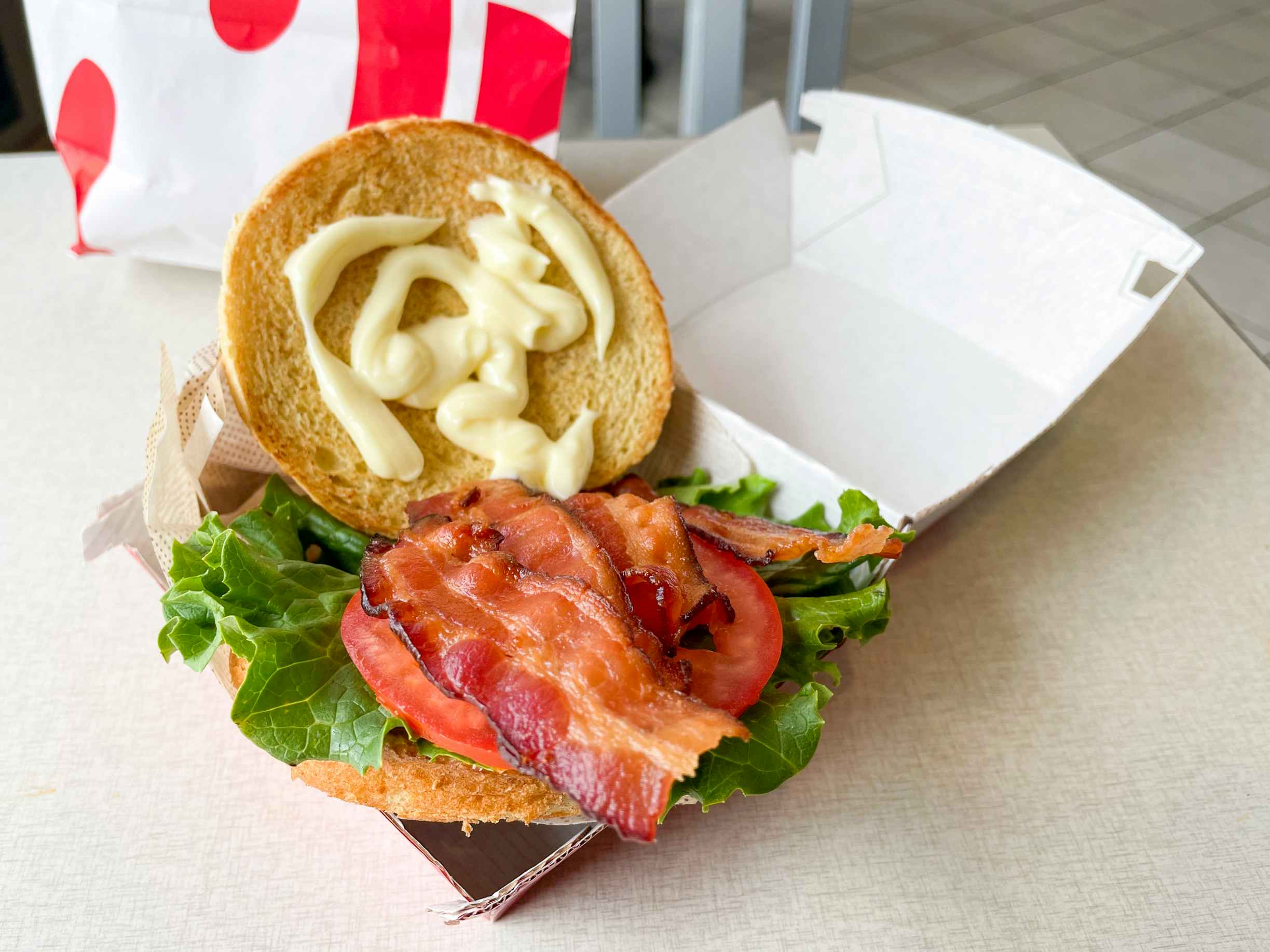 A bacon lettuce tomato sandwich open in a cardboard takeout box from chick-fil-a