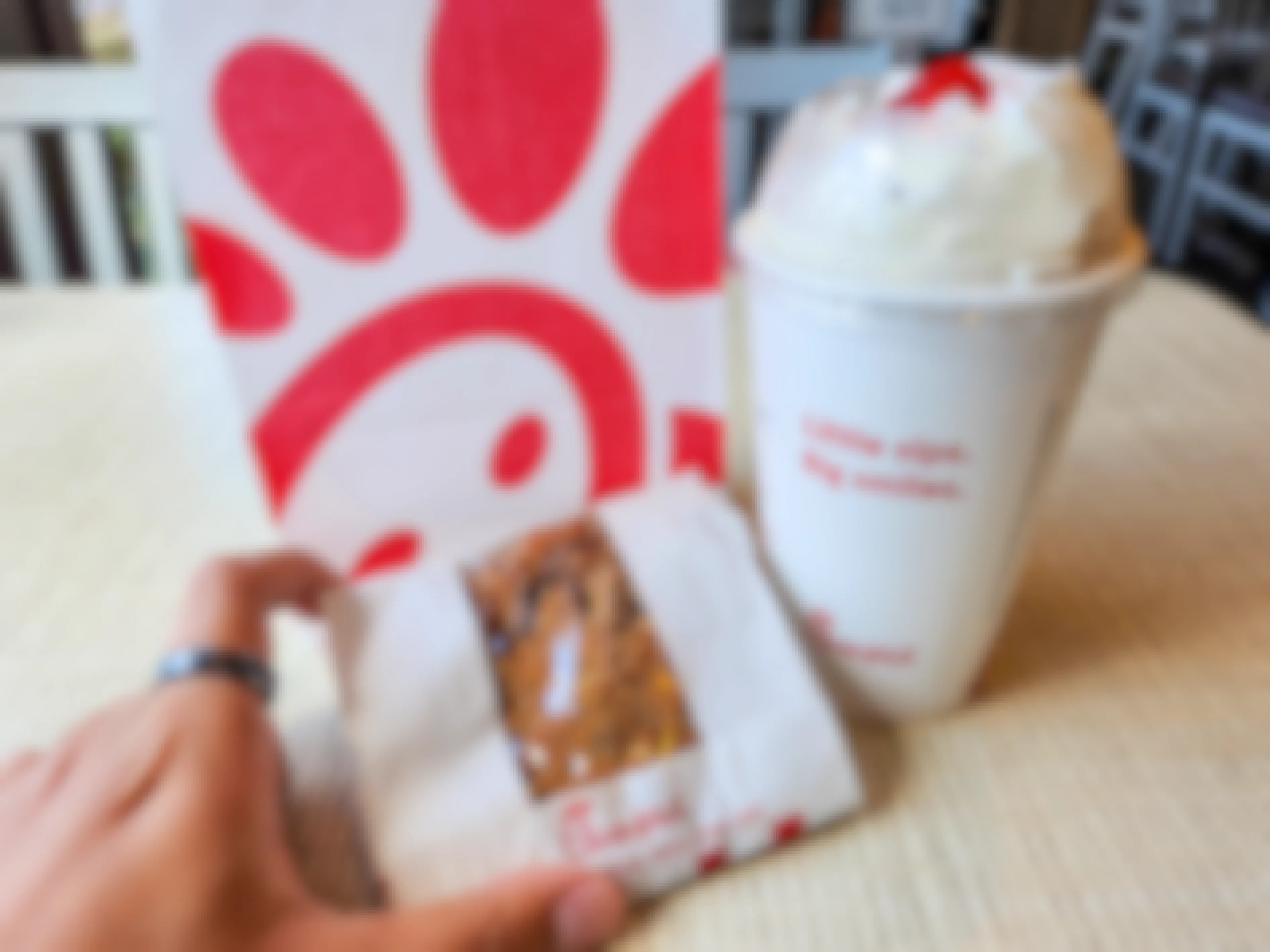 A person's hand picking up a Chick-fil-a cookie from a table next to a milkshake and bag.