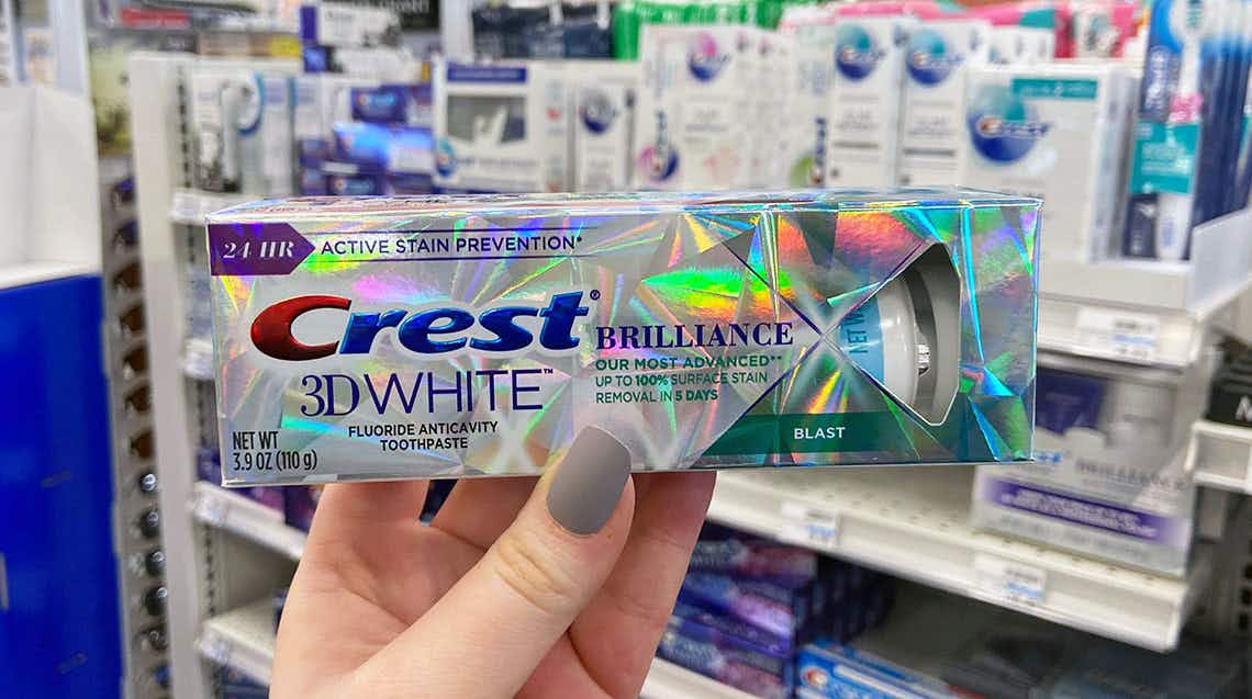 hand holding a tube of crest 3d white brilliance toothpaste in a store