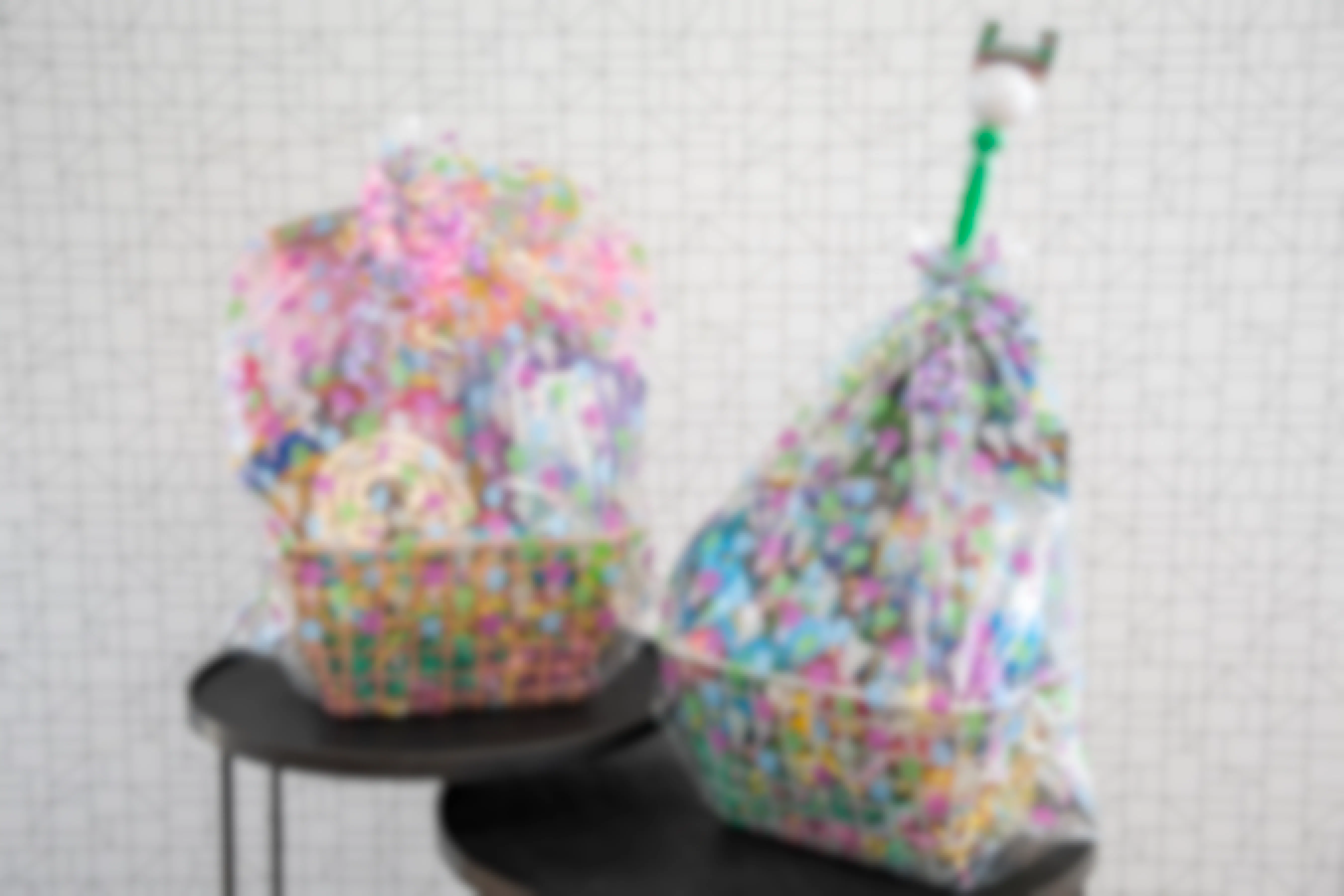 Two large Easter baskets wrapped in Easter themed basket bags sitting on and tables