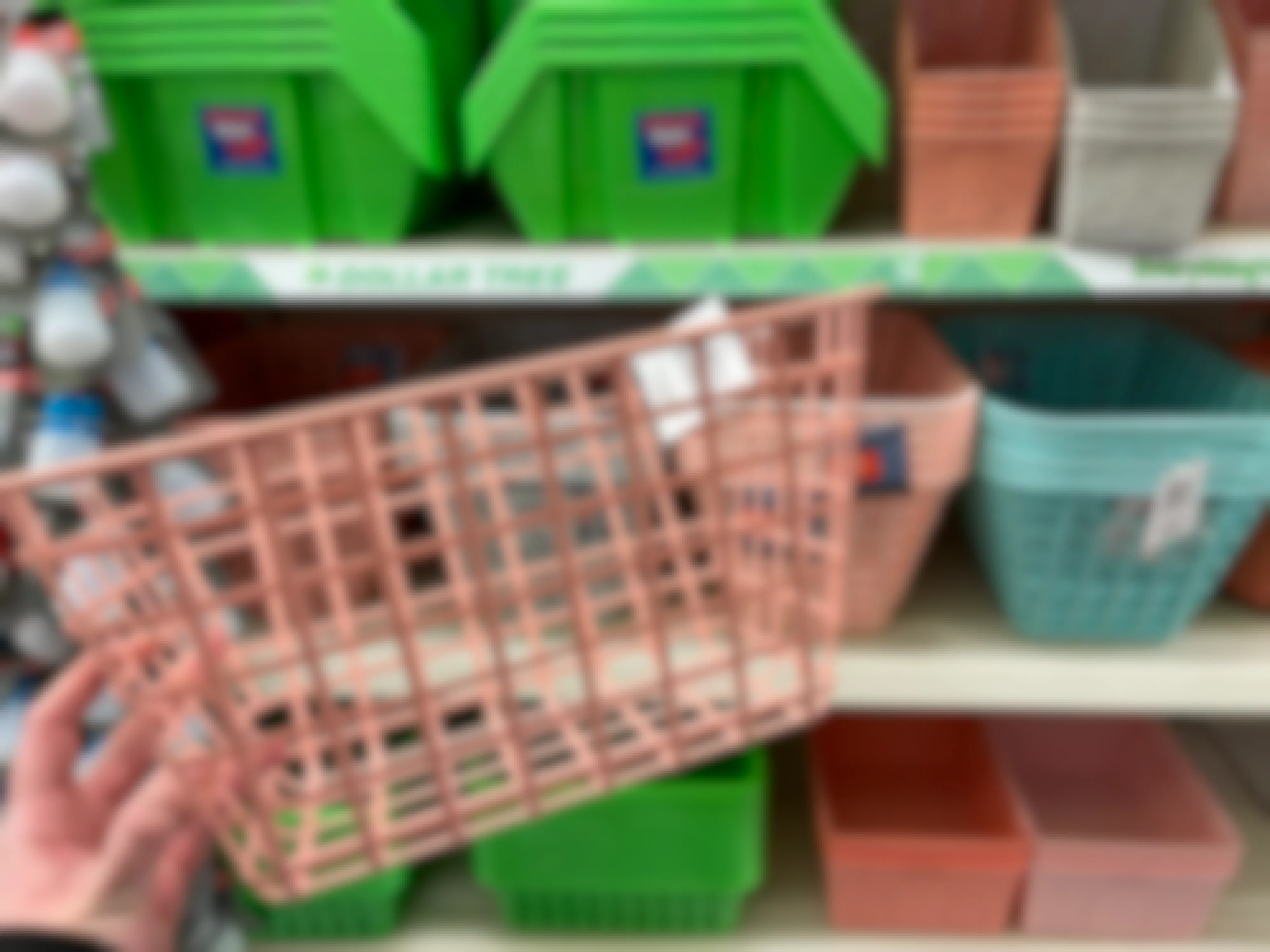 A person holding a pink storage basket in front of a dollar store shelf filled with other storage baskets.