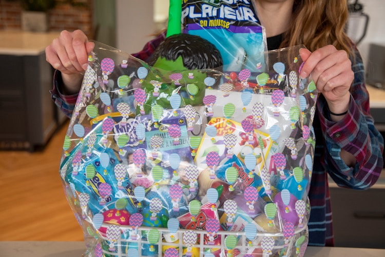 A woman pulls an Easter themed Easter basket bag over a basket filled with items.