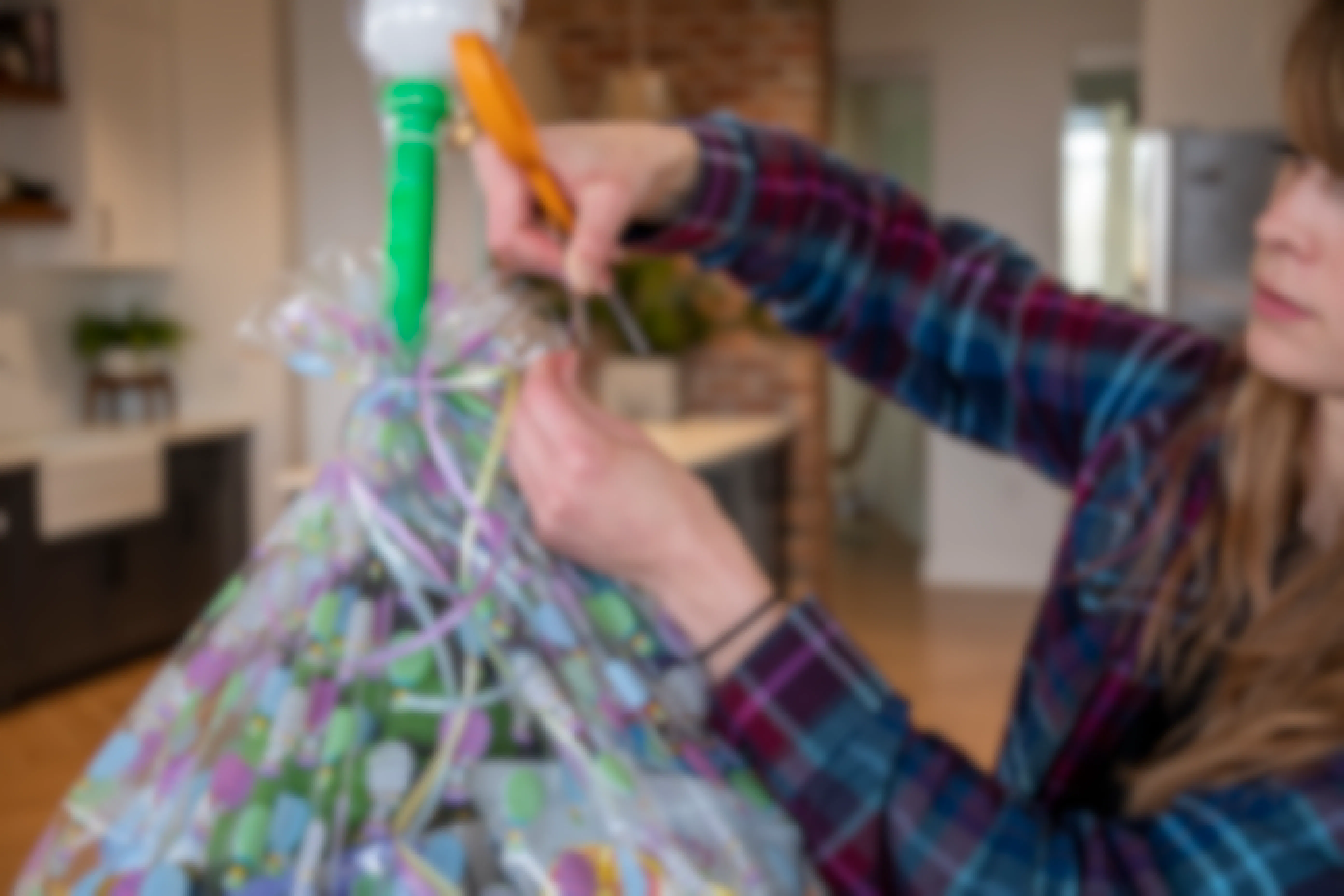 A woman uses orange handled scissors to curl ribbon tied at the top of an Easter basket