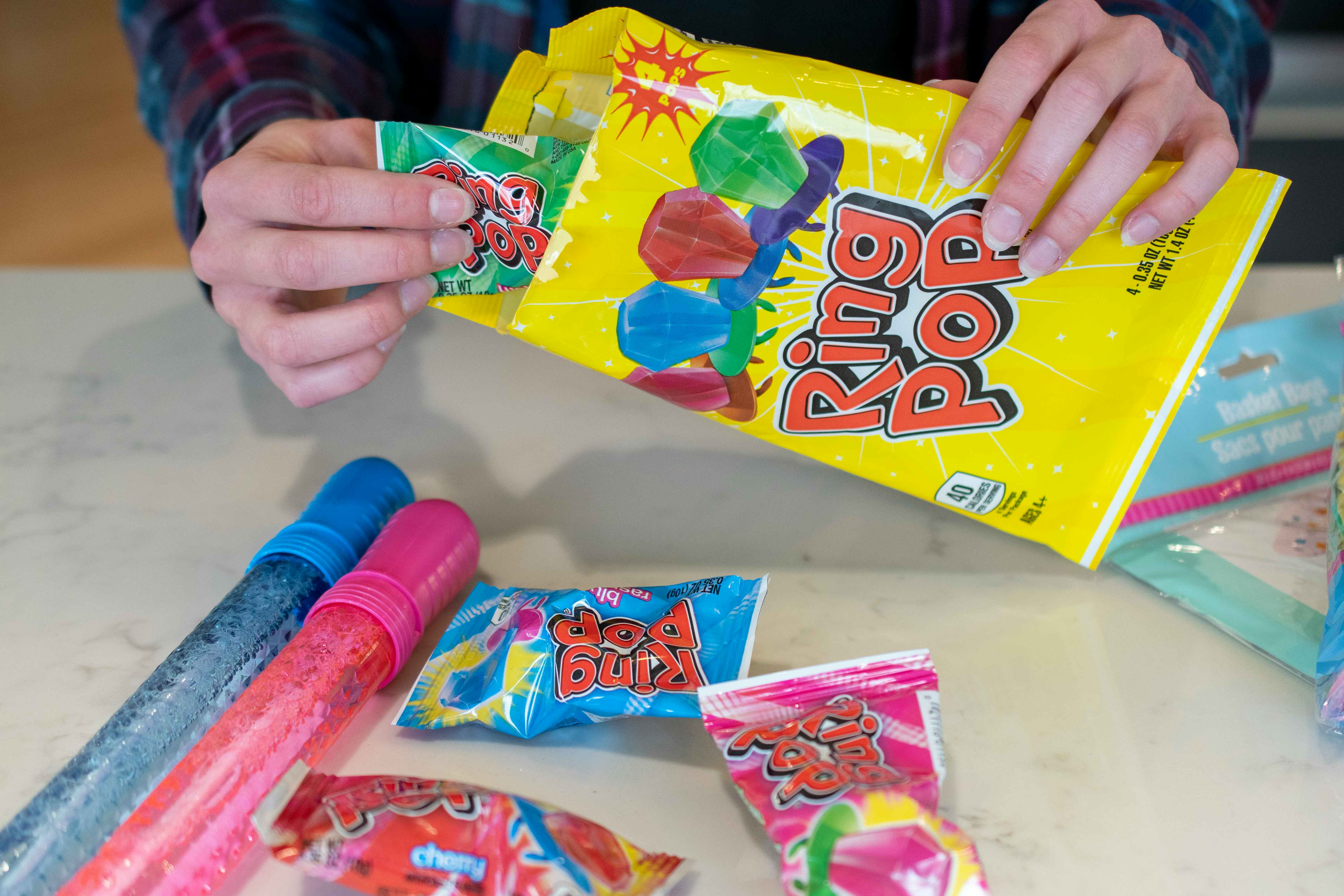 A person pulling a ring pop out of the packaging with three others on the table next to two bubble wands