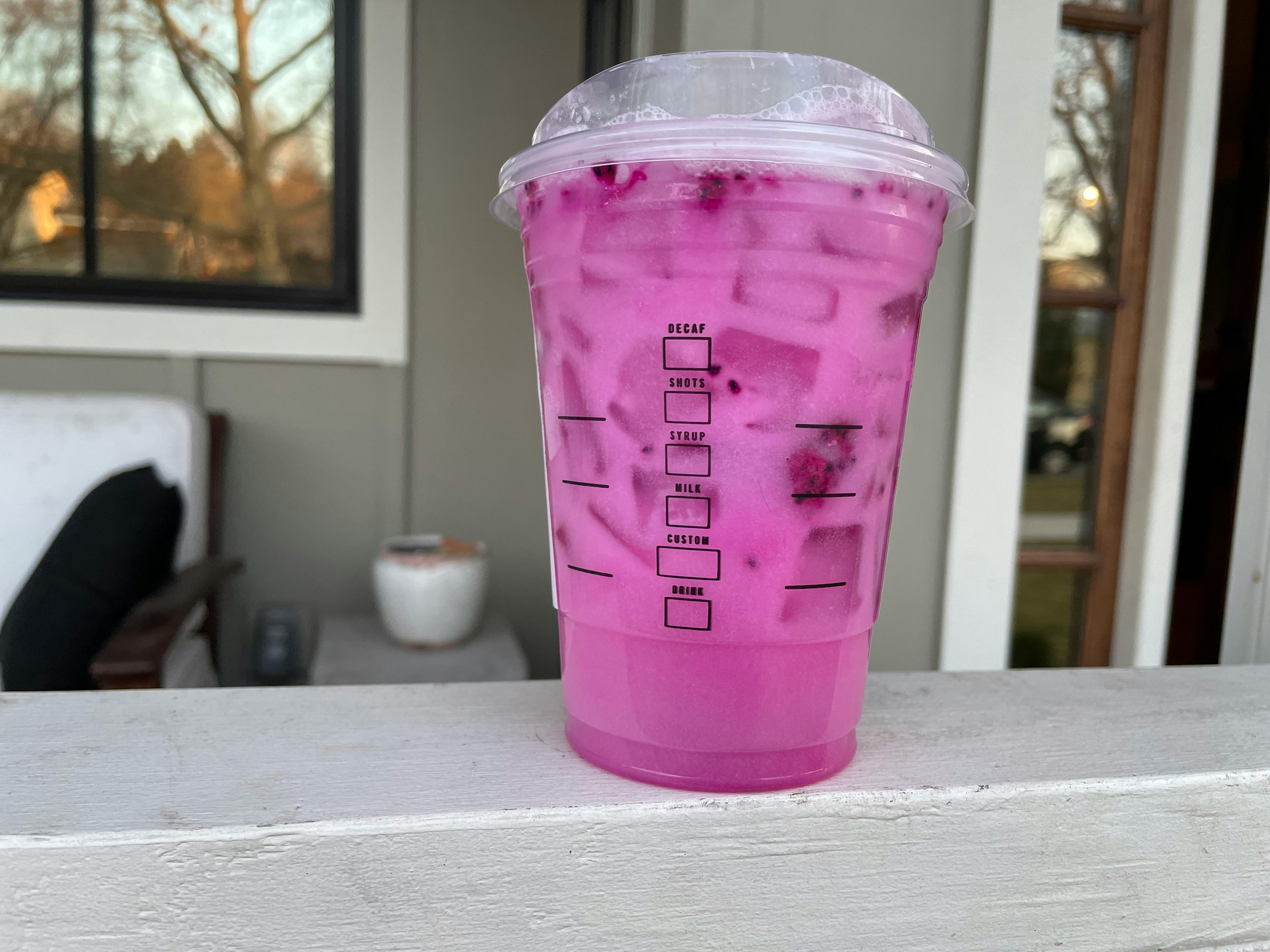 A Starbucks Grande Dragon Drink sitting on the bannister on someone's front porch.