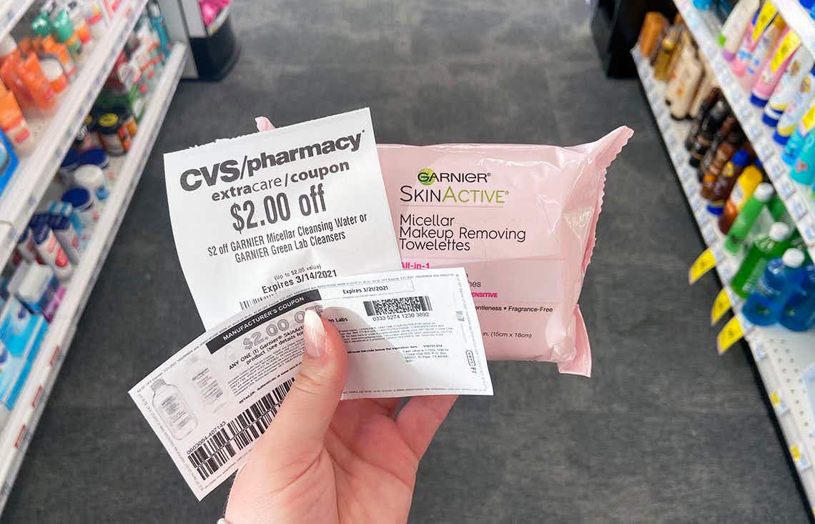 someone holding two $2 coupons and garnier makeup towelettes
