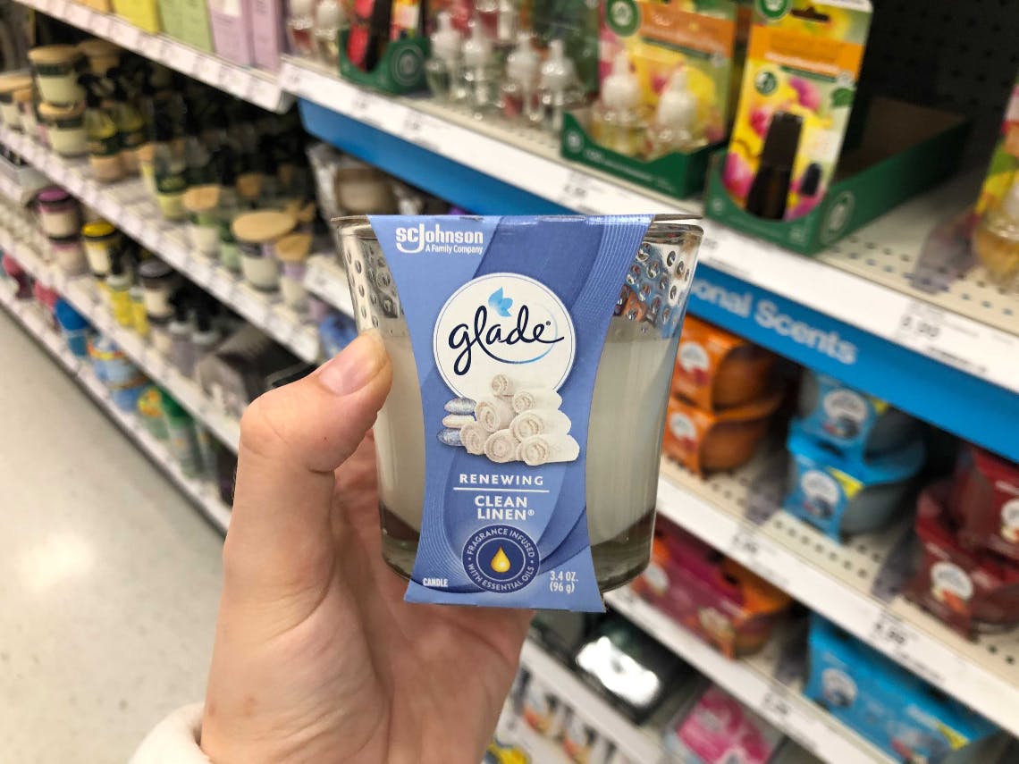 A Glade clean linen candle being held in front of a shelf of candles at Target.