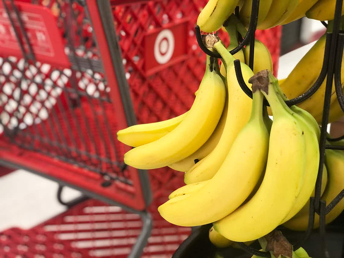 A bunch of bananas hanging from a hook in the produce section with a Target shopping cart visible in the background.
